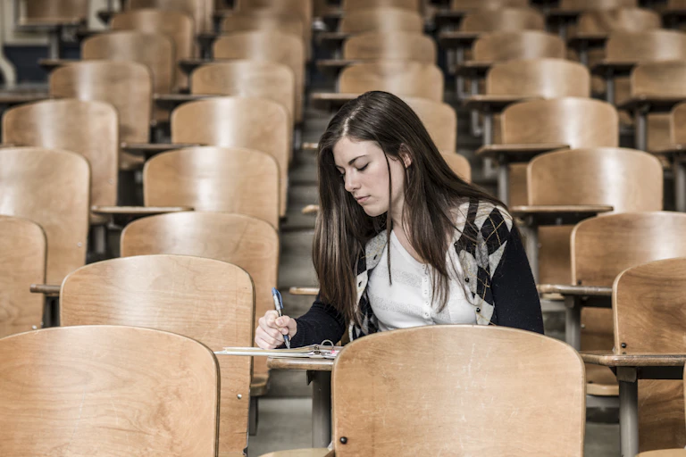 A student sits in a classroom, writing in a notebook.