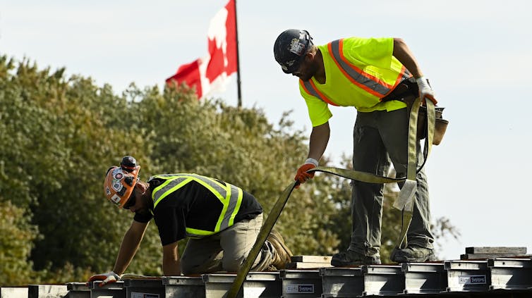 Construction workers on a roof on a sunny day with the Canadian flag flying behind them.
