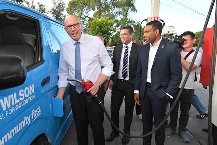 Three men stand next to a car and fill it up with fuel