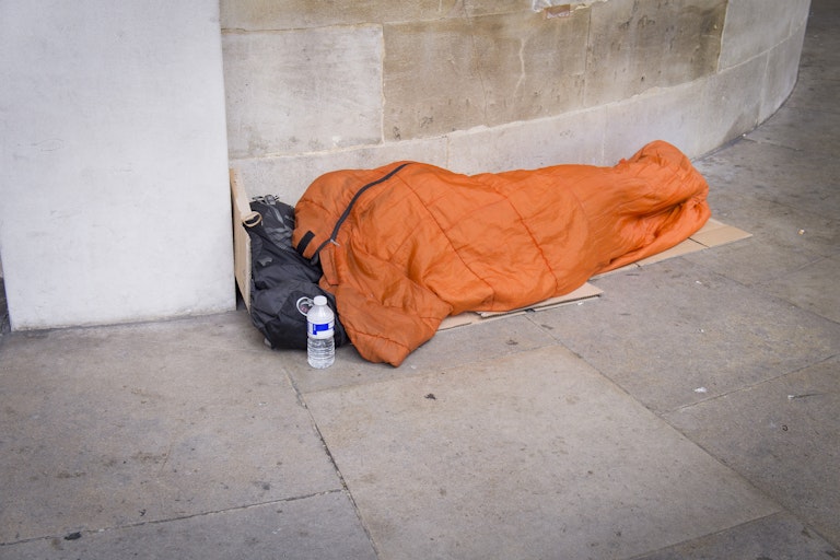 A homeless person in an orange sleeping bag on a footpath