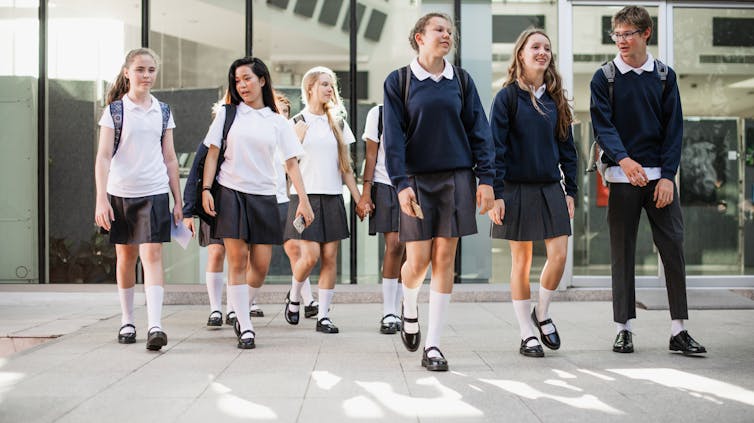 High school students in uniform walk in a group outside a building.