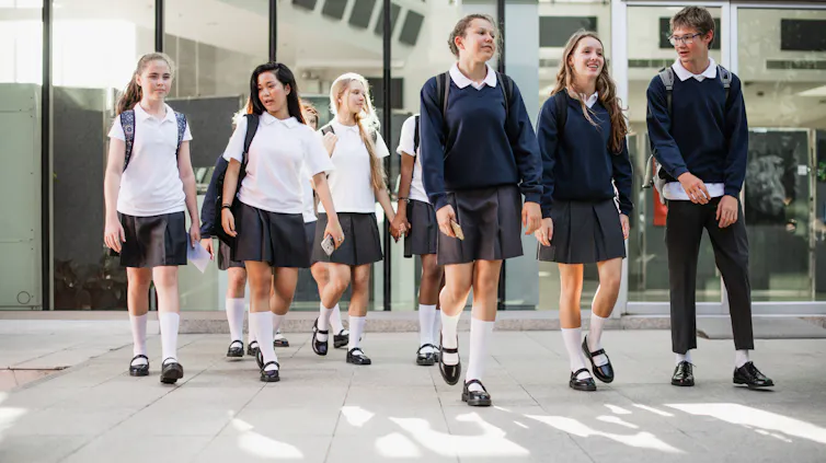 High school students in uniform walk in a group outside a building.