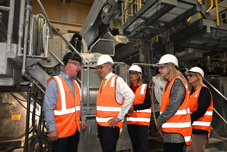 A group of people, including Anthony Albanese, wear high-vis vests and hard hats in a factory