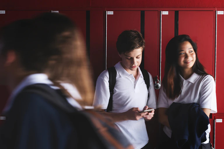 Two students stand next to a row of lockers.