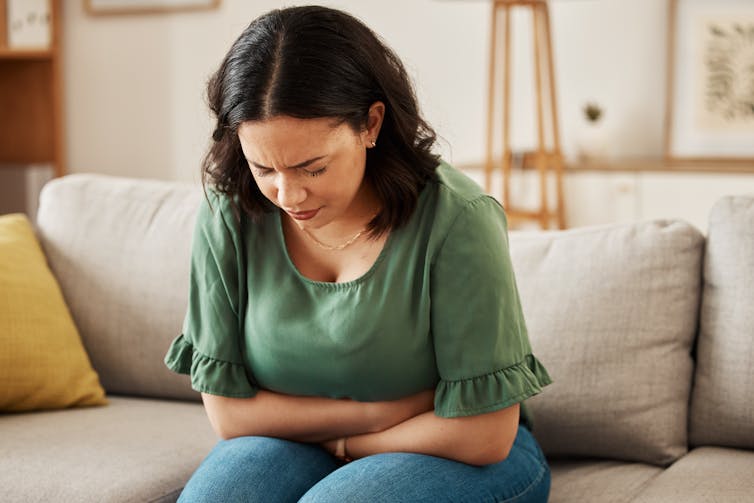 A woman on a couch clutching her stomach.