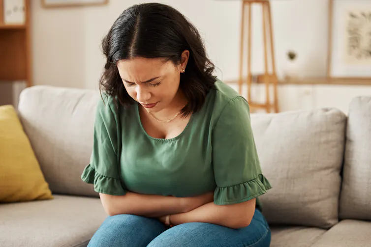 A woman on a couch clutching her stomach.