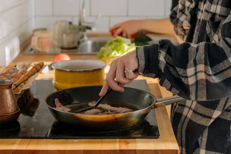 A personal in a flannel shirt cooks on a hob.