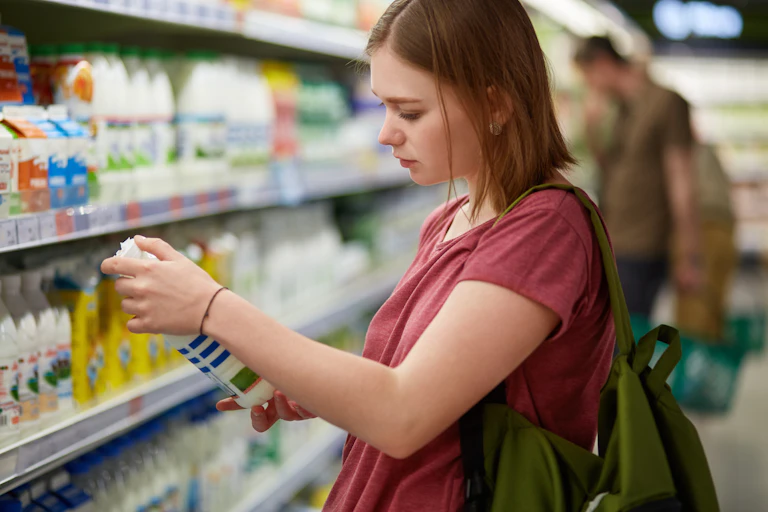 A young woman looks at a bottle of milk in a supermarket daily aisle.