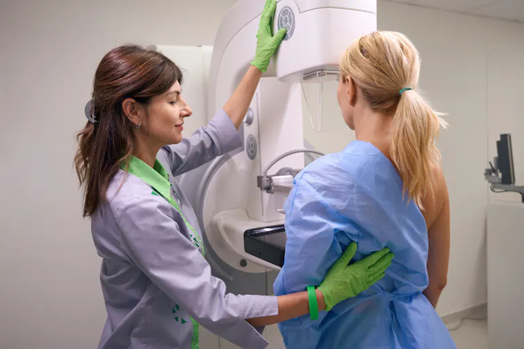 A radiographer prepares a woman for a mammogram, lining her up against the machine.