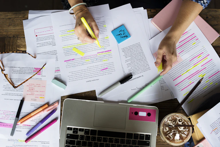 Overhead view of student's laptop and revision notes, with hand holding highlighter