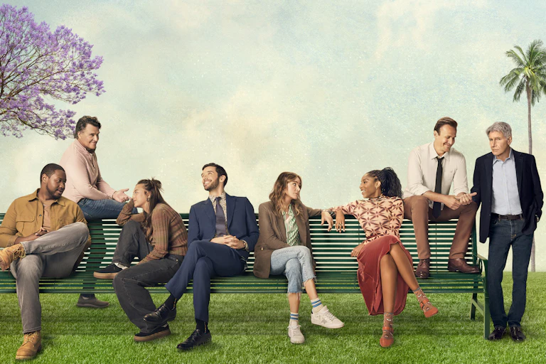 Cast members of a television show sitting on a bench outside.