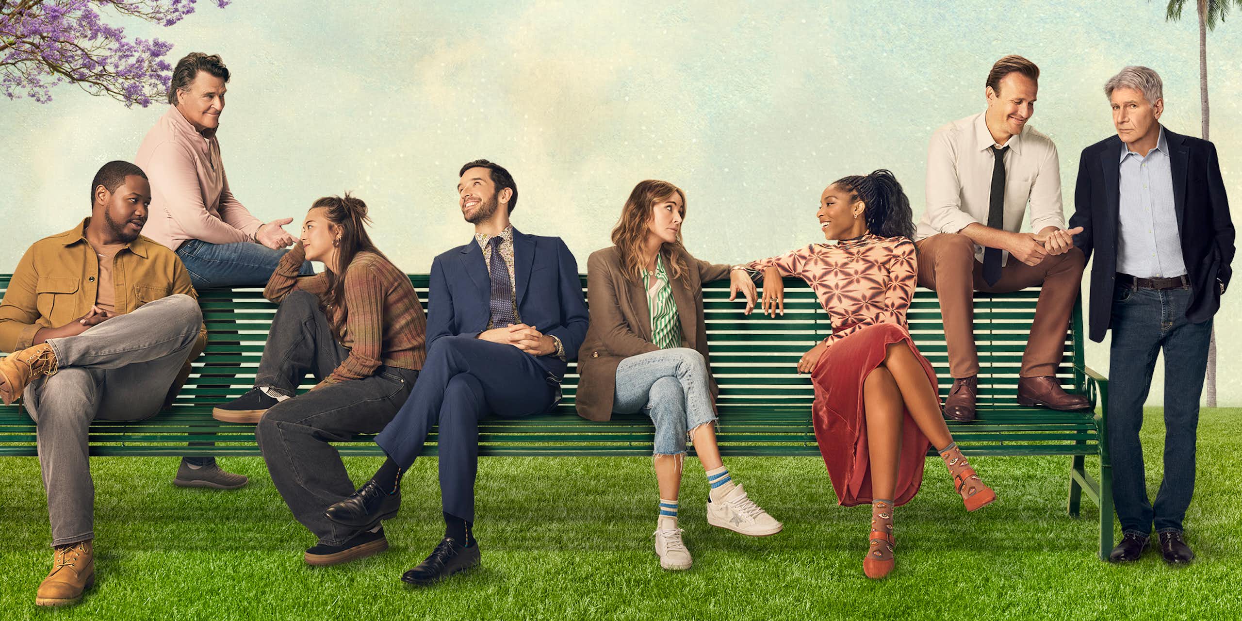 Cast members of a television show sitting on a bench outside.
