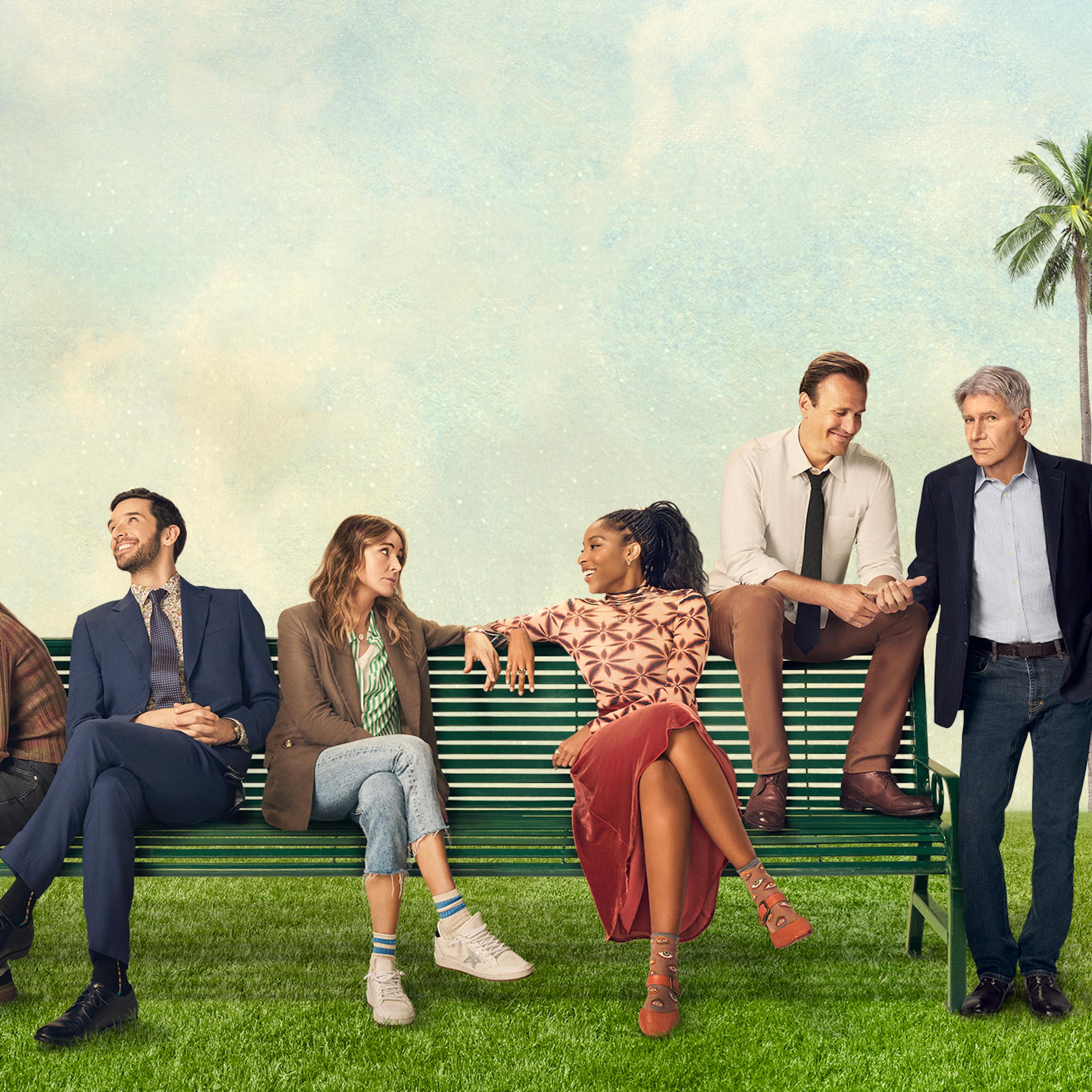 Cast members of a television show sitting on a bench outside.