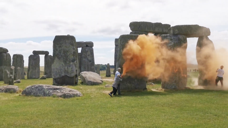 two protesters spray orange substance onto Stonehenge stones.