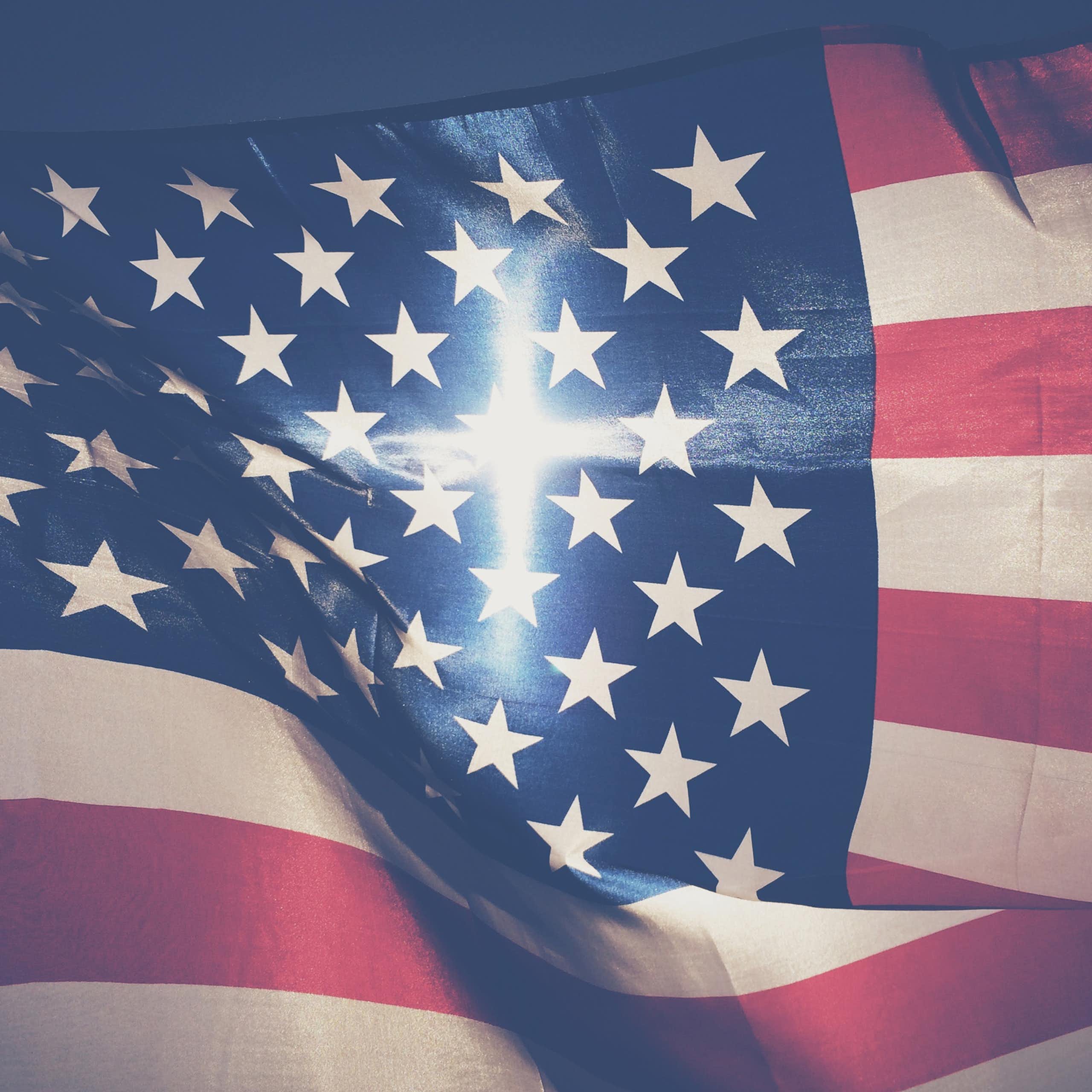An American flag fills the screen, with a cross-shaped beam of light in the center of it.