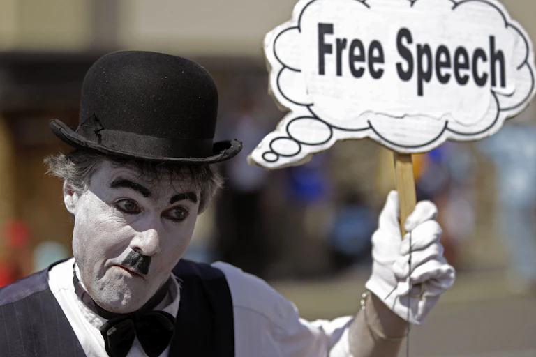 a man wearing white face paint and a bowler hat holds a sign