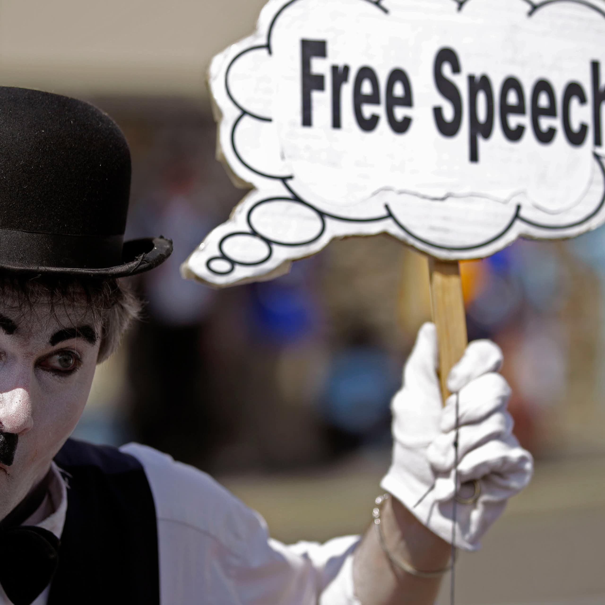 a man wearing white face paint and a bowler hat holds a sign
