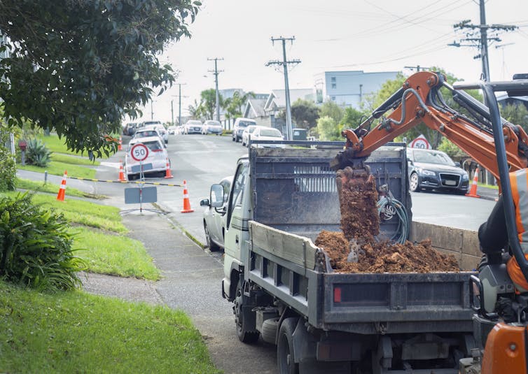 Digger dropping earth into truck on suburban street