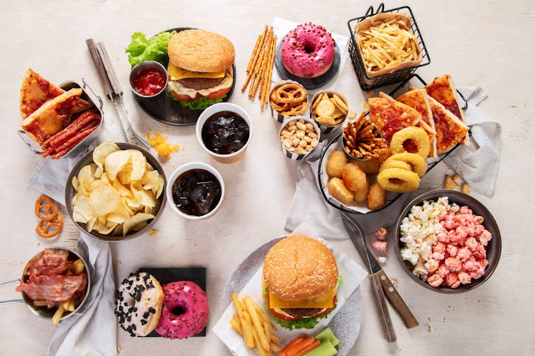 An assortment of processed foods and sugary snacks, included hamburgers, flavoured popcorn, donuts and crisps.