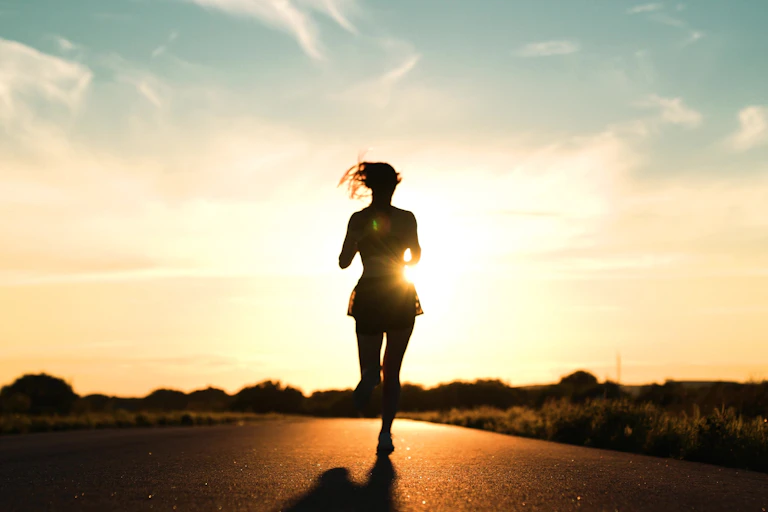 Silhouette of a woman running along a road at sunset.