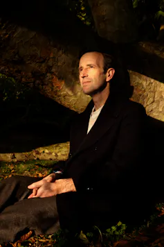 Robert Macfarlane in black suit sat by tree