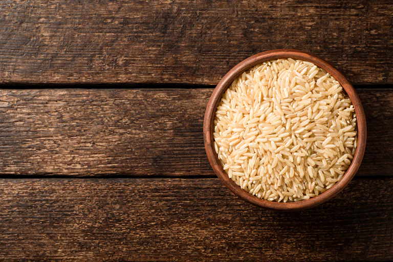 A bowl of uncooked brown rice on a dark wood surface.