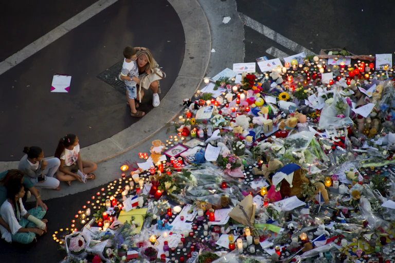 People sit to look at a huge pile of flowers and candles left in memory of victims of an attack in Nice, France.