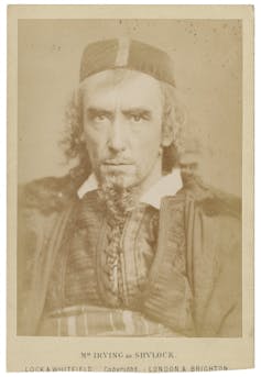 A sepia-toned photograph of a man with a beard, curly hair and cap staring intently at the camera.