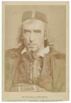 A sepia-toned photograph of a man with a beard, curly hair and cap staring intently at the camera.