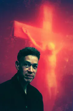 Young man stands in front of an orange and yellow image of a crucifixtion.