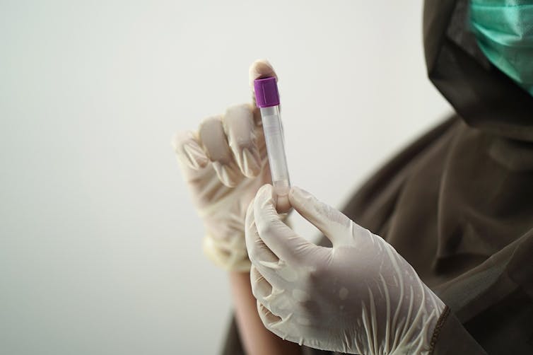 Gloved hands holding a blood sample.