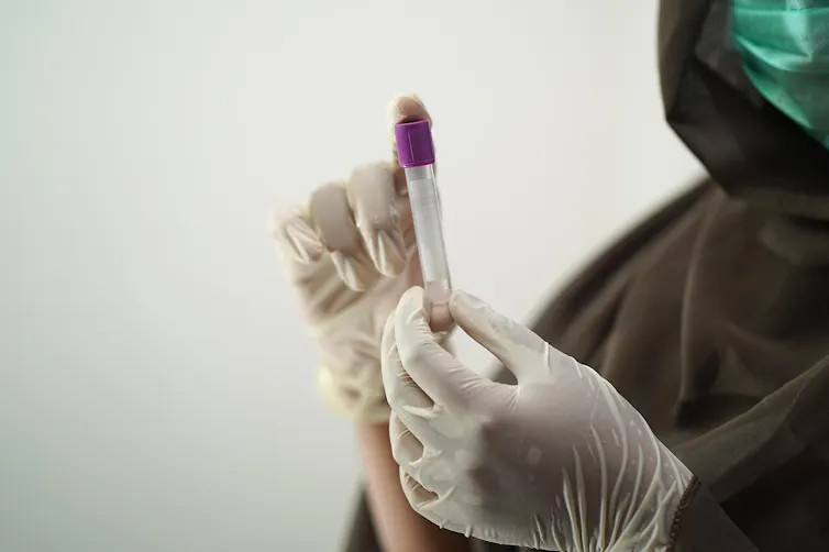 Gloved hands holding a blood sample.