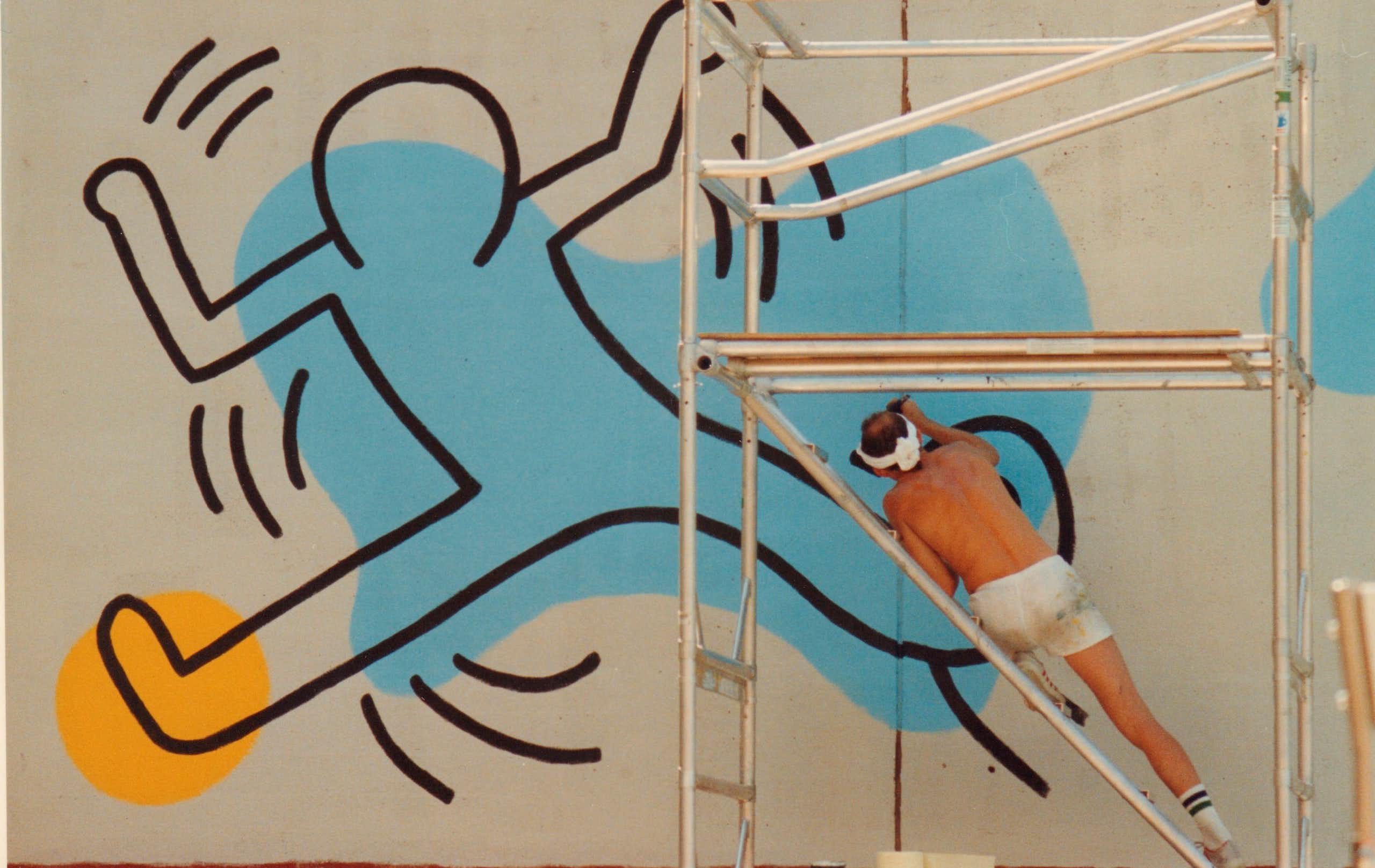 Man paints a large blue and yellow outline of a cartoon person on a wall.