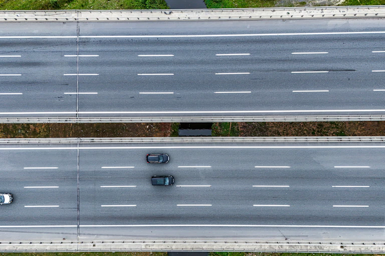 A four-lane highway shown from overhead with a divider and four cars driving on it.