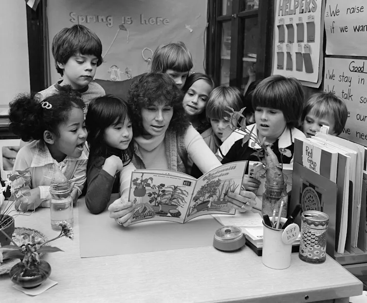 Students gather around a teacher who reads a picture book.