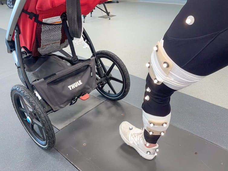 A person holding a stroller and runs forward, and the shot focuses on the front leg when he hits the ground. Their leg is covered with white dots and has a fabric for capturing movement around it.