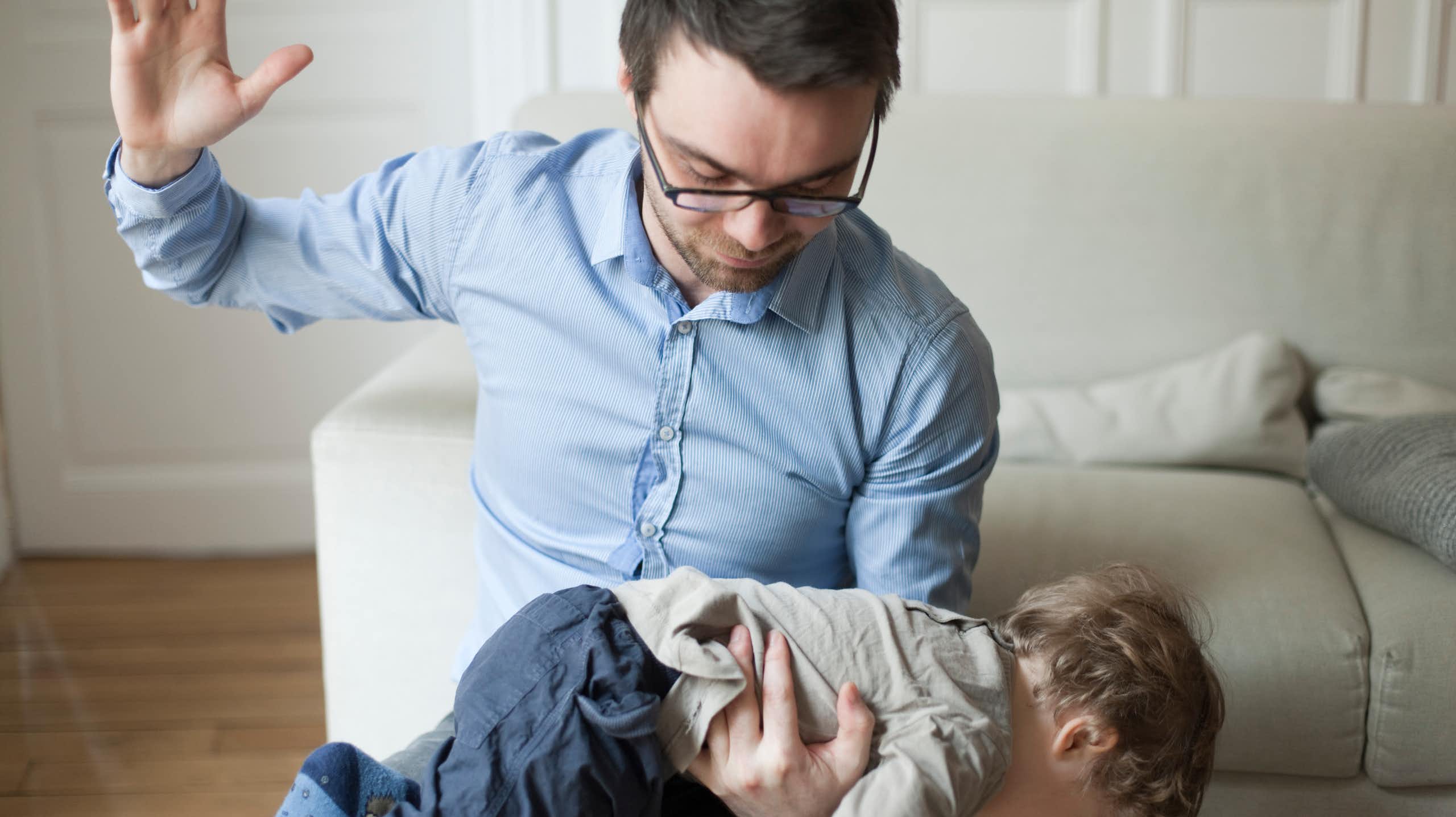 Father raising his hand as if to spank a child that is laid over his lap.