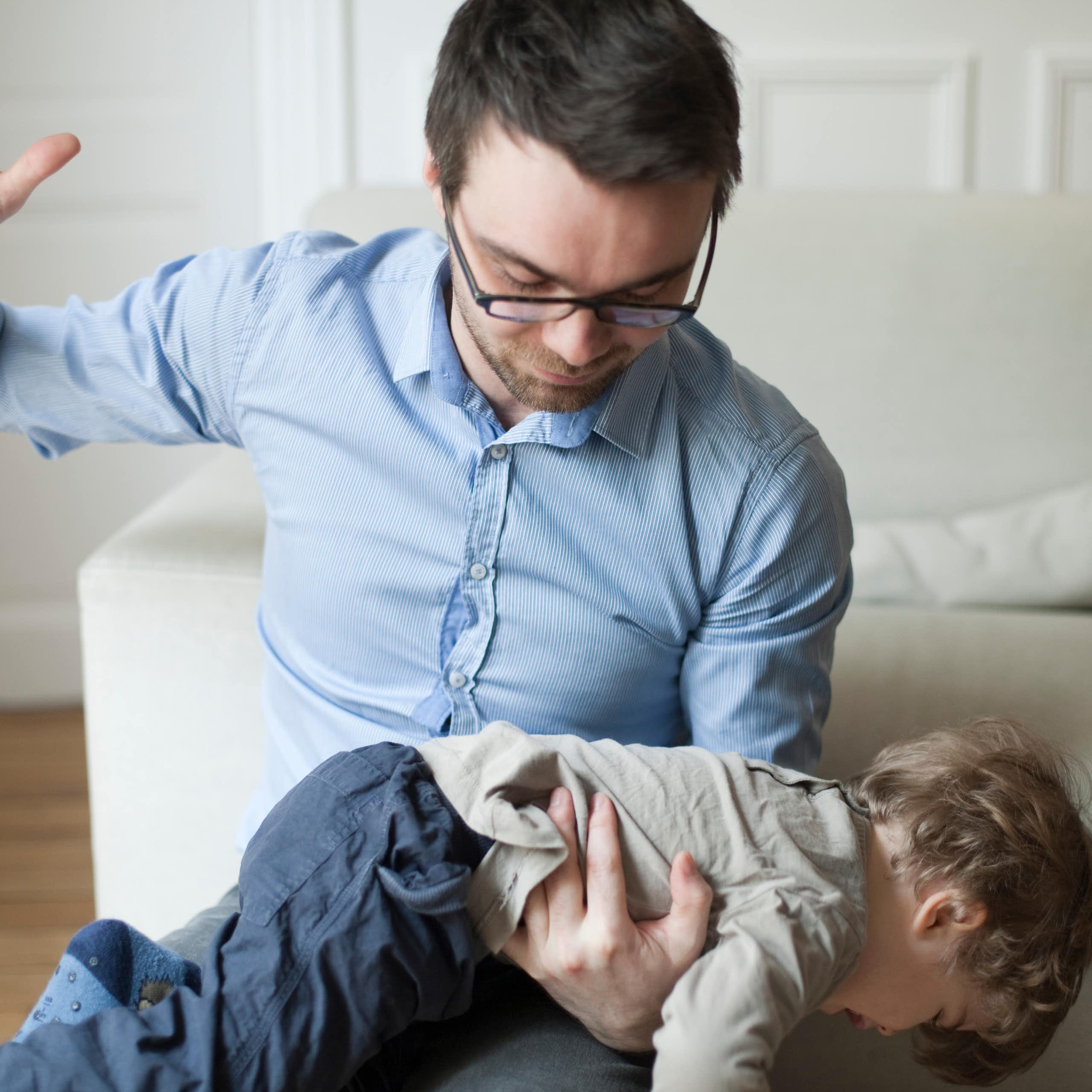 Father raising his hand as if to spank a child that is laid over his lap.