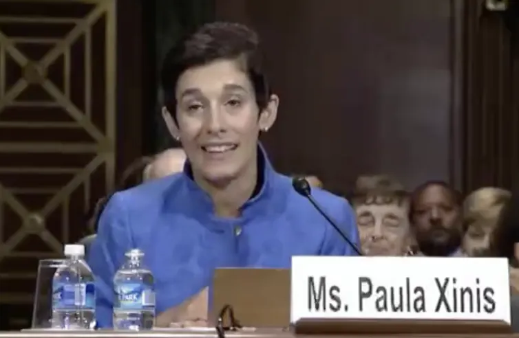 A woman with dark, short hair sitting in front of a microphone, with two water bottles on the table in front of her.