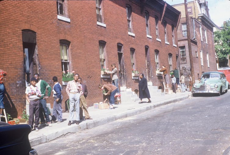 Students and adults shown working on window garden boxes on a block of two-story brick row homes