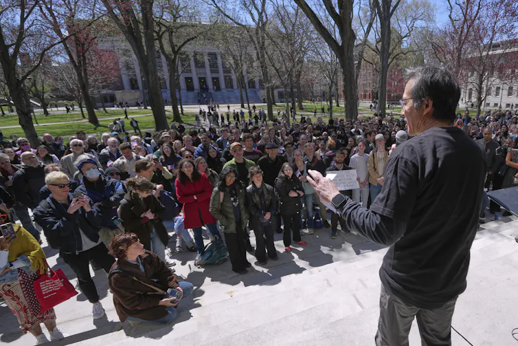 A large group of people gather around a speaker at an outdoor event.