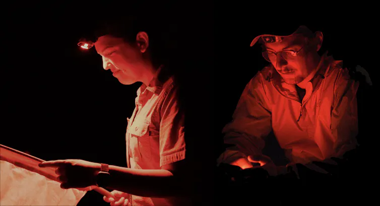 Two people at work in the dark with faces illuminated by red lights.