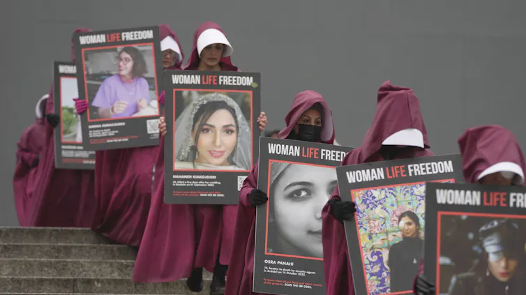 Women dressed in red Handmaid's Tale robes carry the photos of women killed in Iran.