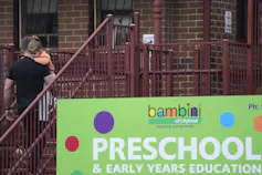 Australia's increase in child-care fees has far exceeded the increase in consumer prices since the 1990s. A man carries a child up steps next to a sign that says preschool.