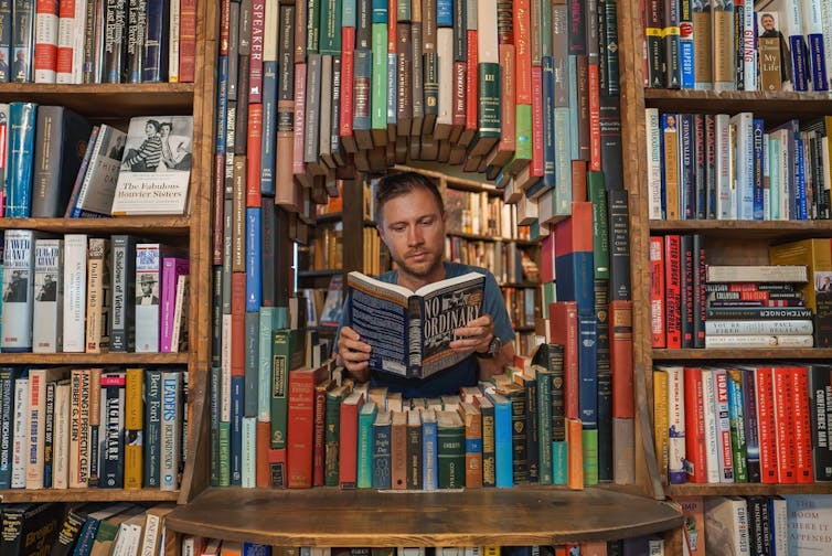 Un hombre lee un libro titulado 'No Ordinary' a través de un túnel circular de libros en The Last Bookstore, Los Ángeles