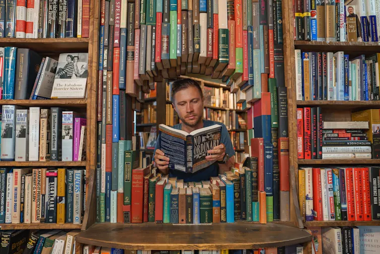 Un hombre lee un libro titulado 'No Ordinary' a través de un túnel circular de libros en The Last Bookstore, Los Ángeles