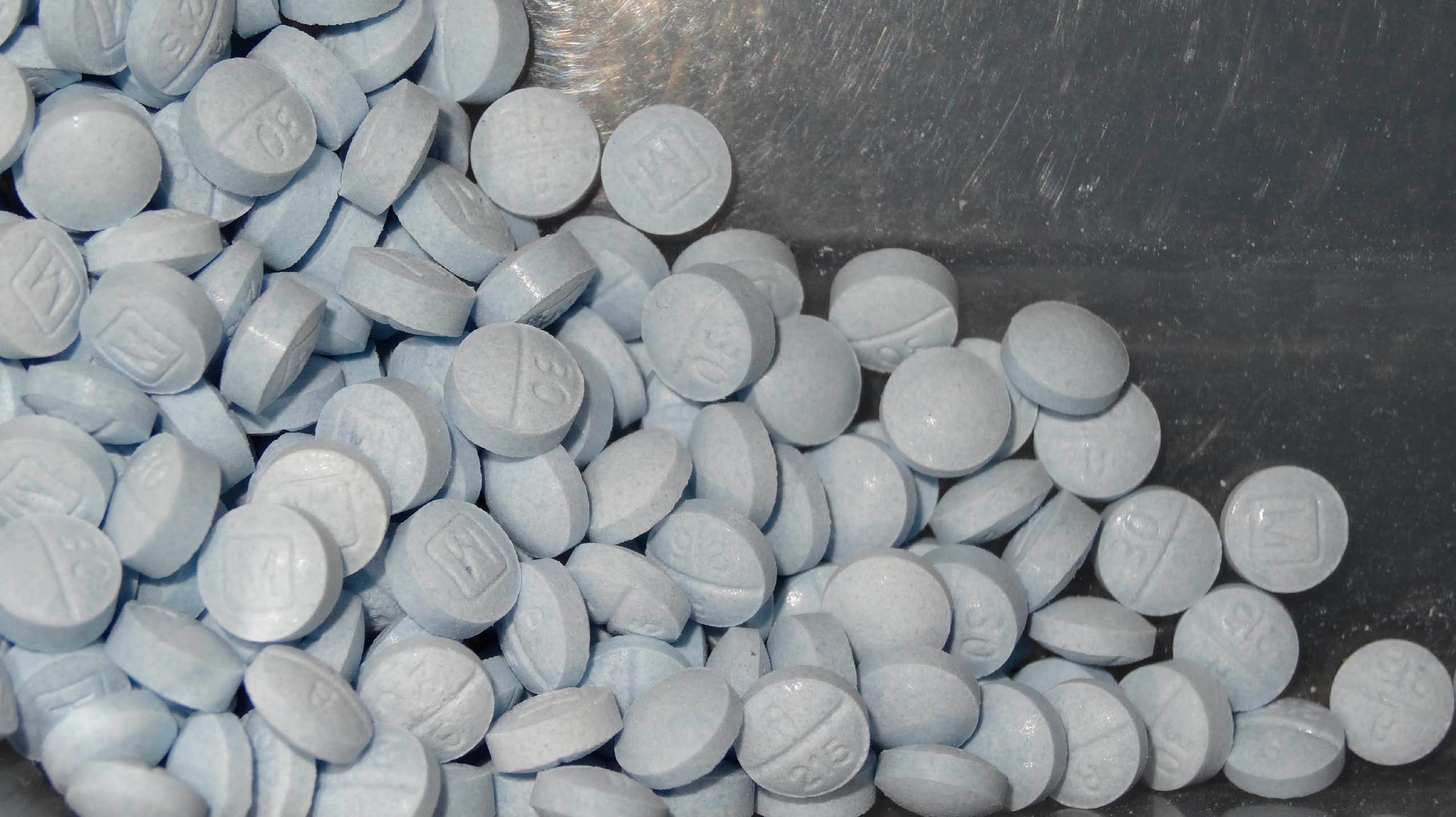 A pile of round blue pills against a chrome background