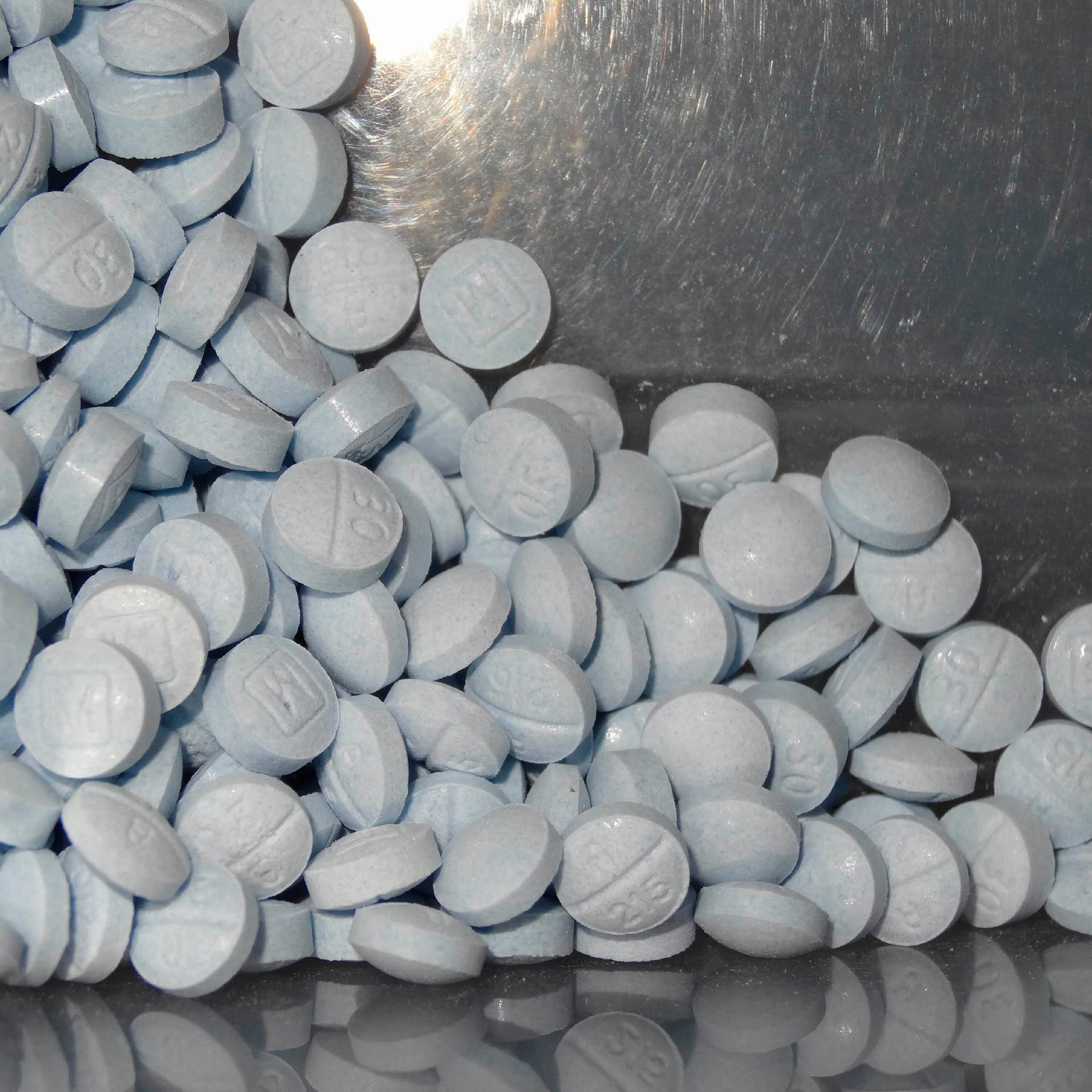 A pile of round blue pills against a chrome background
