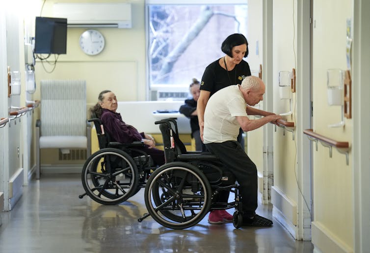 El trabajador de cuidado ayuda a un hombre mayor que se extiende frente a su silla de ruedas.