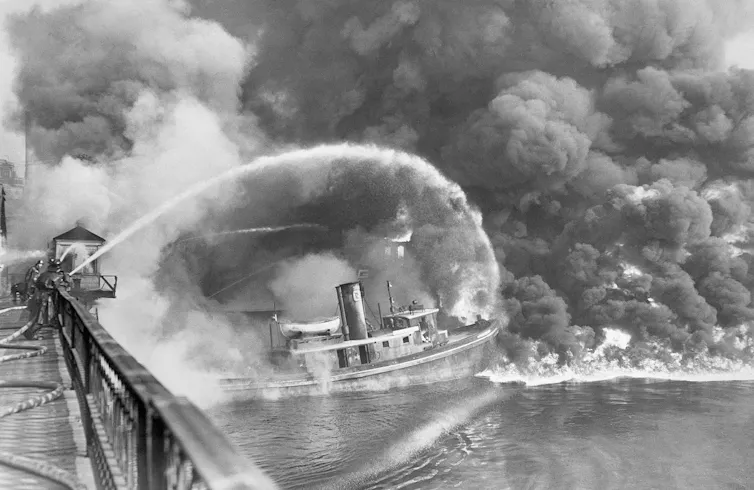 Firemen stand on a bridge over the Cuyahoga River to spray water on the tug Arizona, as a fire, started in an oil slick on the river